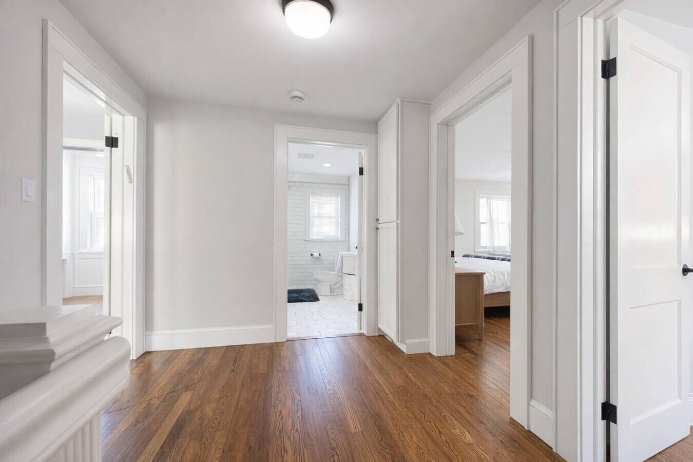 A hallway with wooden flooring, white walls, and doors leading to a bathroom and a bedroom.