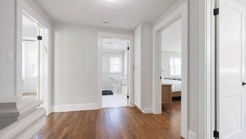 A hallway with wooden flooring, white walls, and doors leading to a bathroom and a bedroom.