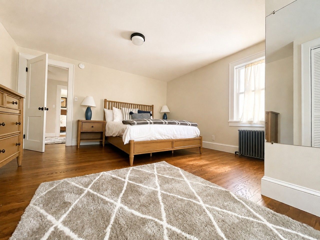 A bedroom with a bed, bedside tables, a dresser, and a radiator.
