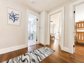 Un couloir doté d’un plancher en bois, de murs blancs et d’un tapis à motifs de marbre.