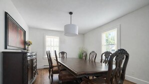 A dining room with a large wooden table, six chairs, a dark wooden cabinet, and a hanging light fixture. - Enclosed Hot Tub, King Bed, 3 bdrm, close to town (Ellenville)