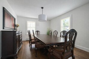 Une salle à manger avec une grande table en bois, six chaises, un buffet en bois foncé et un luminaire suspendu.