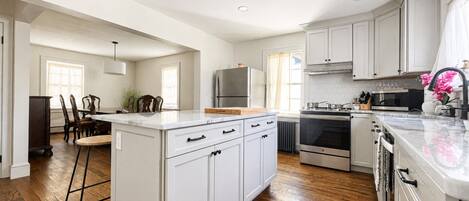 Una cocina moderna con armarios blancos, una isla central y un comedor con sillas de madera.