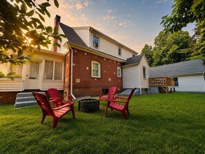 Il s’agit d’une propriété résidentielle comprenant une maison en briques, un garage blanc et une cour verdoyante agrémentée de chaises Adirondack rouges.