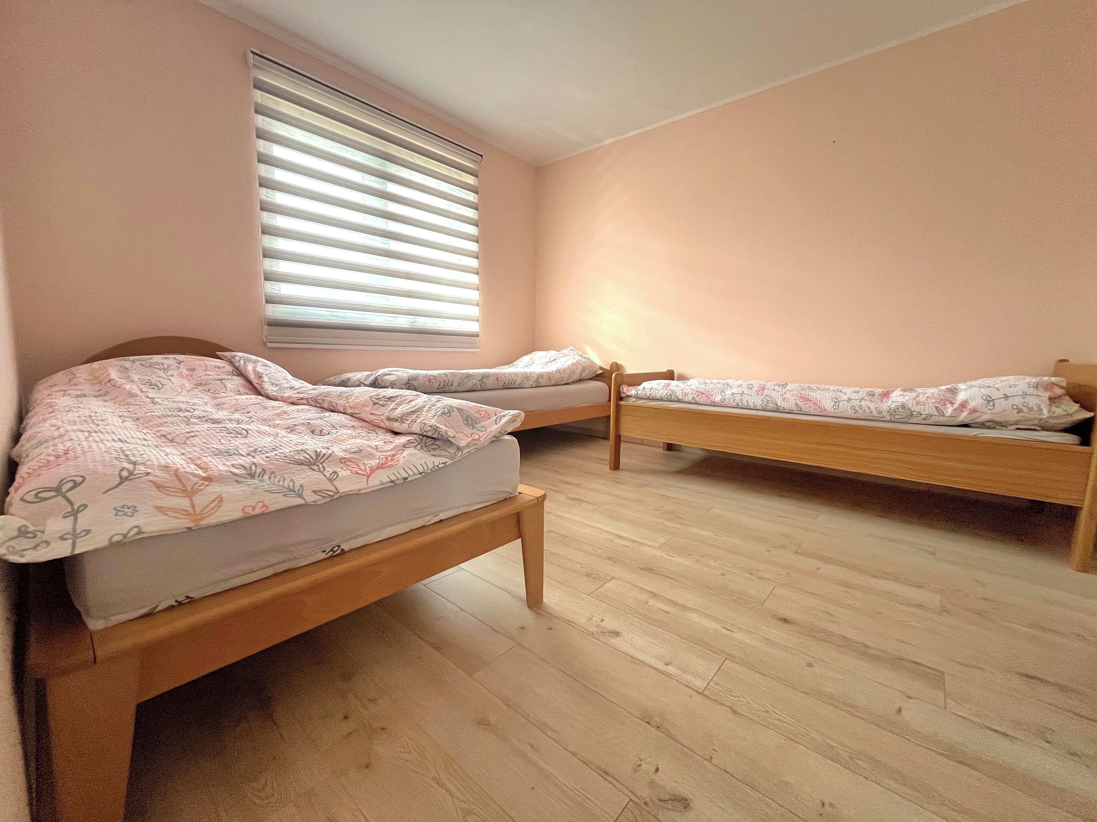 A room with two wooden beds, a window with blinds, and a wooden floor.