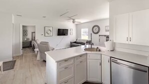 A modern kitchen with white cabinetry, a built-in dishwasher, and a large island with a sink. - Cottage on Dona Bay (Nokomis)