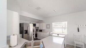 A modern kitchen with white cabinetry, stainless steel appliances, and a central island with a sink. - Cottage on Dona Bay (Nokomis)