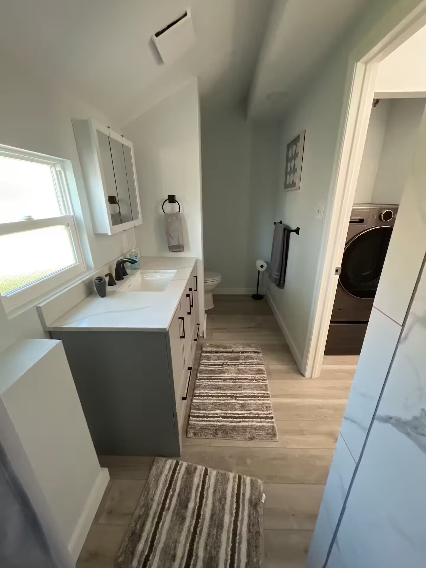 Une salle de bain moderne dotée d’un grand lavabo, de toilettes et d’un espace douche. Une fenêtre laisse entrer la lumière naturelle et un porte-serviettes est placé au-dessus du lavabo.