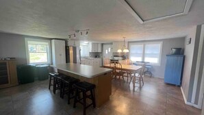 A spacious kitchen with a large island, bar stools, a dining table with chairs, and a blue cabinet. - Lakefront Retreat w/ Private Dock • Sleeps 8 (Mecosta)
