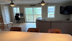 A living room with a sofa, a dining table with chairs, a TV, and a ceiling fan. - Lakefront Retreat w/ Private Dock • Sleeps 8 (Mecosta)