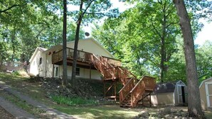 A two-story house with a wooden staircase leading to a balcony. - Lakefront Retreat w/ Private Dock • Sleeps 8 (Mecosta)