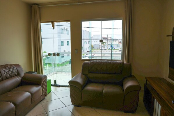 A living room with two sofas, a large window with a view of buildings and a street, and a television on a wooden stand.