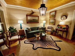 Una sala de estar acogedora con un sofá verde, un tapete de zebra, muebles de madera y obras de arte enmarcadas en las paredes.