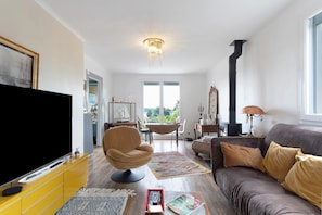 Ein Wohnzimmer mit Fernseher, Sofa, Sessel und einem Essbereich mit Tisch und Stühlen.