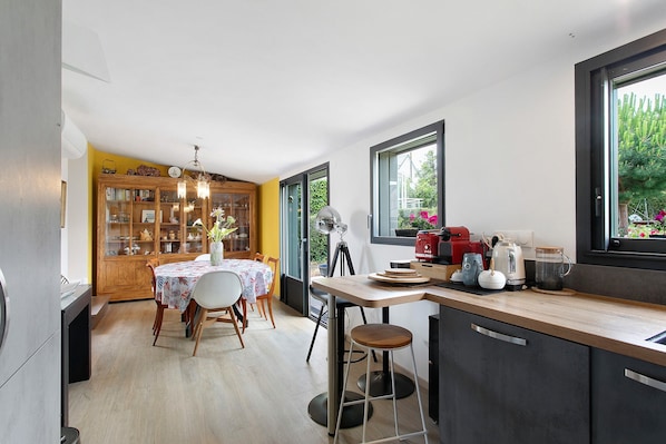 A modern kitchen with a dining area, wooden cabinets, and a view of greenery outside. - Holiday Home “Penn Ar Bed” with Sea View, Wi-Fi and Air Conditioning (Paimpol)