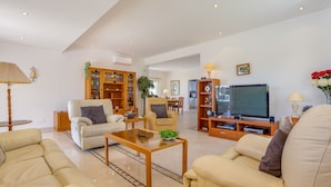Ein geräumiges Wohnzimmer mit einer Couch, Sesseln, einem Couchtisch und einem Fernseher.