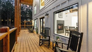 A wooden deck with outdoor seating and a fireplace visible through a large window. - Pancakes & Sausage | Hot Tub • Slide • Game Loft (Broken Bow)
