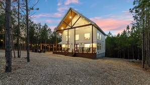 A two-story log cabin with a covered porch and a gravel driveway. - Pancakes & Sausage | Hot Tub • Slide • Game Loft (Broken Bow)