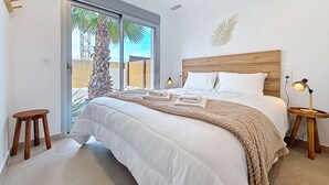 Camera da letto con un letto grande, testiera in legno e vista su palme attraverso la porta in vetro.