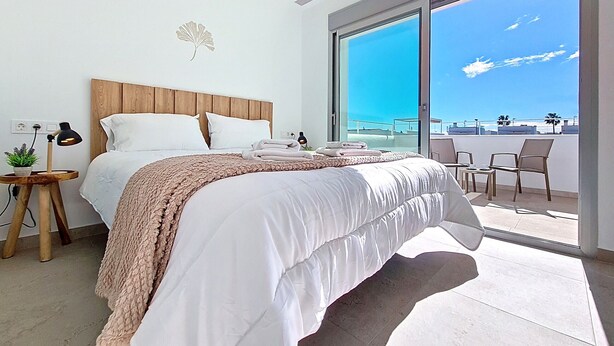 Una camera da letto moderna con un letto grande, una testata in legno, un comodino con una lampada e vista sull'oceano tramite una porta scorrevole in vetro.