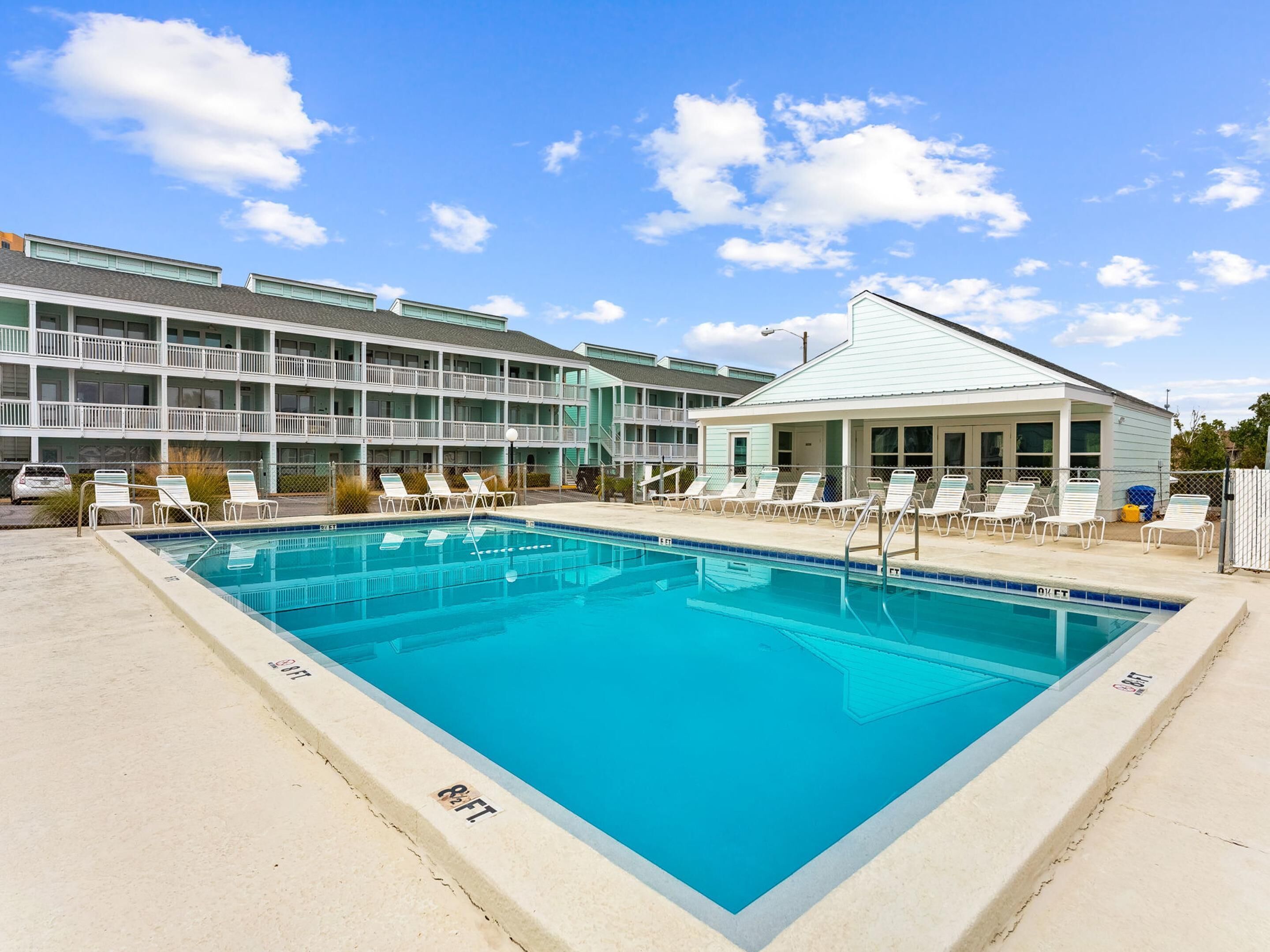 Une piscine rectangulaire, dotée de chaises longues, et un bâtiment avec de nombreux balcons en arrière-plan.