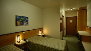 A hotel room with two single beds, a bedside table with a lamp, a painting on the wall, a desk with a chair, and a bathroom door. - park hotel morotin (Santa Maria)