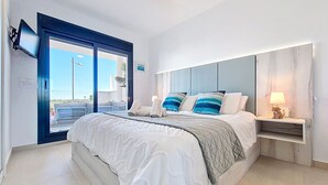 Ein Schlafzimmer mit einem großen Bett, einem Deckenventilator, einem an der Wand montierten Fernseher und Blick ins Freie durch eine Schiebetür.