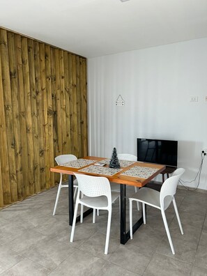 A dining area with a wooden table, white chairs, a small Christmas tree, and a television on the wall. - Apart Maipu (Maipú)