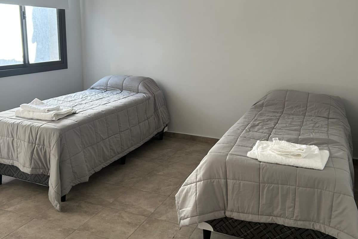 A room with two beds, each with a quilted bedspread and pillows, and a window providing natural light.