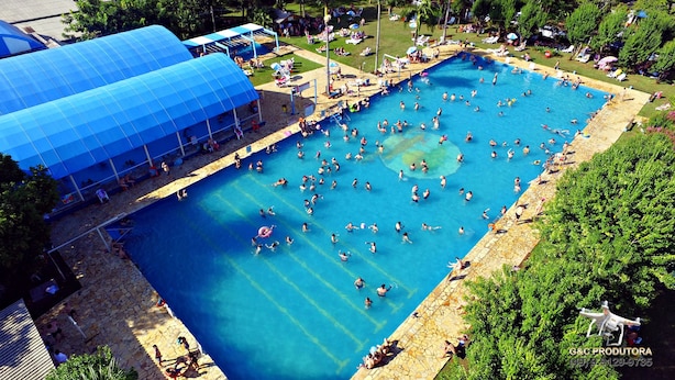 A large outdoor swimming pool surrounded by lounge chairs and umbrellas, with a covered area to the left. - Pousada Praia Verde - Ilha Redonda | Palmitos-SC (Palmitos)