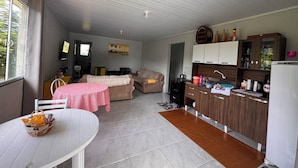A compact living space with a kitchenette, a dining area with a table and chairs, a sofa, and a TV. - Pousada Praia Verde - Ilha Redonda | Palmitos-SC (Palmitos)
