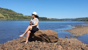 A person sitting on a rock by a calm lake with a clear sky. - Pousada Praia Verde - Ilha Redonda | Palmitos-SC (Palmitos)