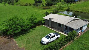 A modern house with a large front yard, a driveway, and a white pickup truck parked in front. - Pousada Praia Verde - Ilha Redonda | Palmitos-SC (Palmitos)