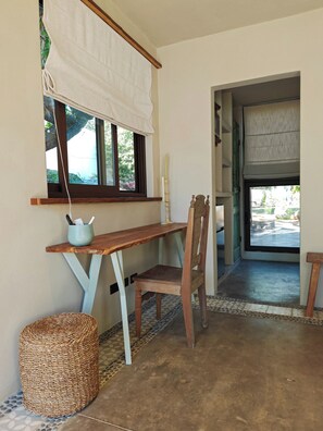 Une pièce avec un bureau en bois, une chaise, un panier en osier et une fenêtre ornée d’un rideau blanc.