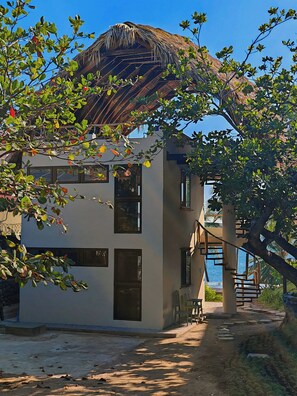 A building with a thatched roof, a staircase leading to a balcony, and a view of the sea.