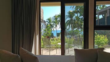 A hotel room with a bed, a view of the ocean, and a balcony with chairs and plants.