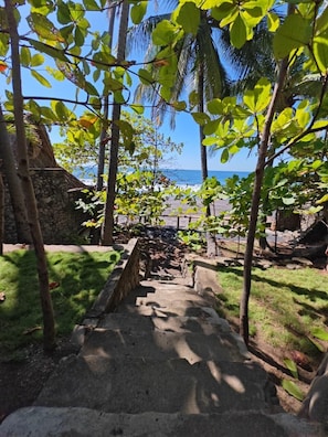 Eine Steintreppe führt zu einem Strand mit Palmen und freiem Blick auf den Ozean.
