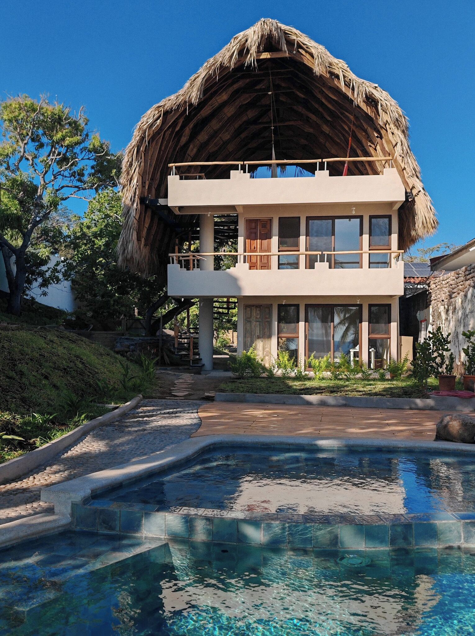 A two-story building with a thatched roof, a swimming pool, and a garden area.