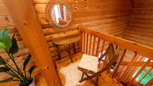 Interior acogedor de una cabaña con paredes de madera, un banco de madera, un sillón blanco con cojín, un espejo y una planta en maceta.