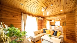 Interior de una cabaña de troncos con sala de estar, sofá, mesa de centro y área de cocina.