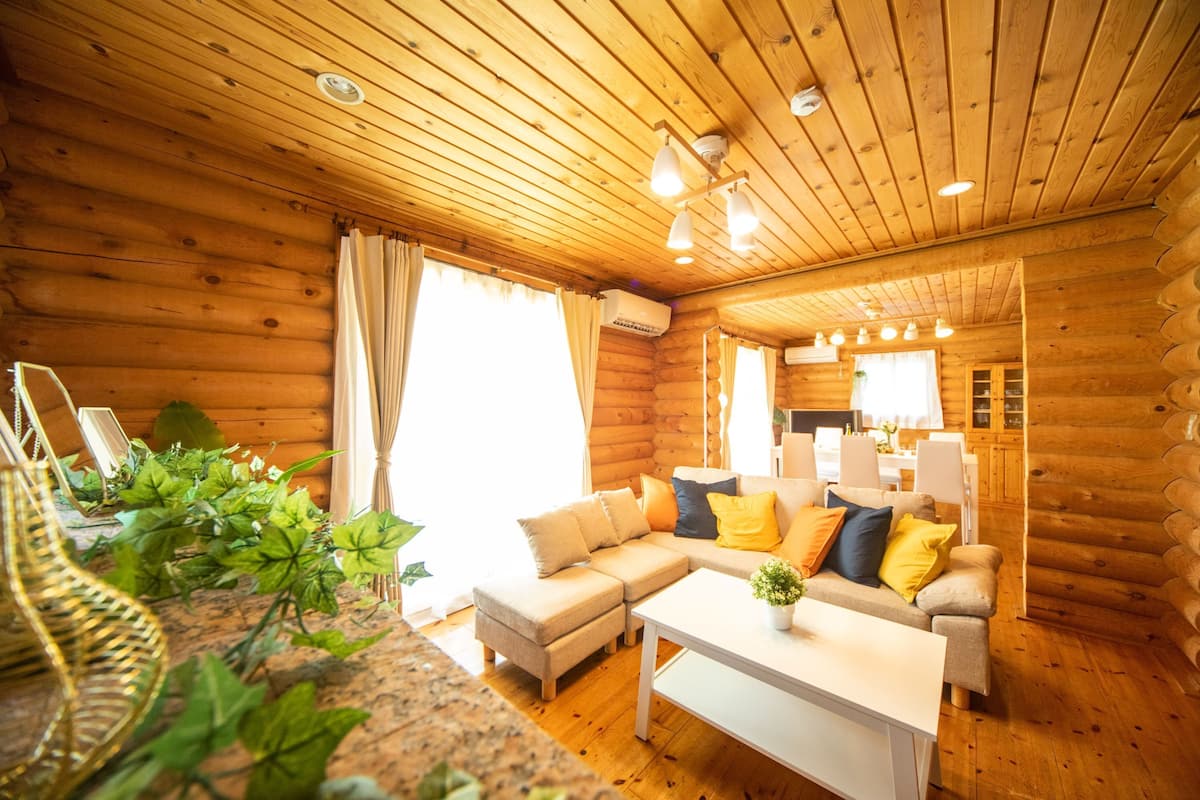 A log cabin interior with a living room, sofa, coffee table, and a kitchen area.