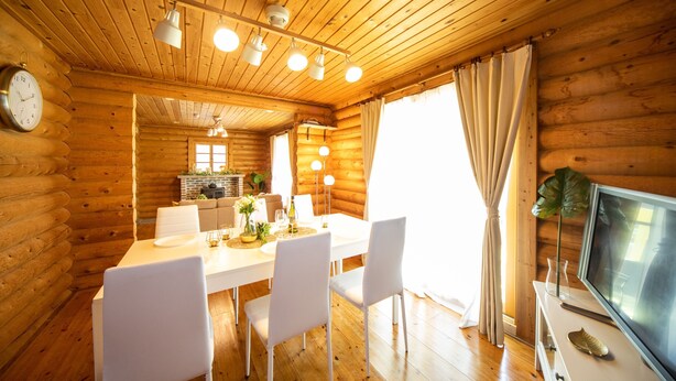 Interior de una cabaña de madera con comedor, cocina y televisor.