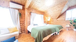 Habitación tipo cabaña de madera con cama, sofá, una mesita y una planta en maceta.
