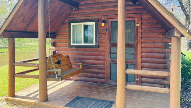 A wooden cabin with a porch, a swing, and a welcome sign.