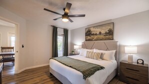 A bedroom with a bed, bedside tables, a ceiling fan, a painting, and a window with curtains. - Stonecreek Golf Condo | Heated Pool & Spa (Scottsdale)