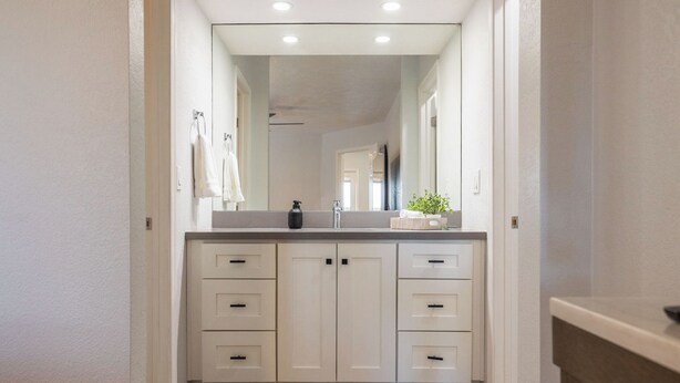 A narrow hallway leading to a bathroom with a white vanity, a mirror, and a plant on the counter. - Stonecreek Golf Condo | Heated Pool & Spa (Scottsdale)