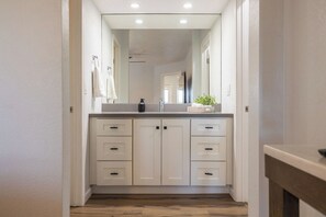 A narrow hallway leading to a bathroom with a white vanity, a mirror, and a plant on the counter. - Stonecreek Golf Condo | Heated Pool & Spa (Scottsdale)