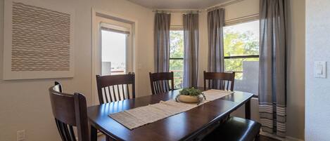 A dining room with a wooden table, four chairs, a bench, a plant centerpiece, and a textured wall art piece.