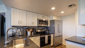 A modern kitchen with stainless steel appliances, a black countertop, and white cabinetry. - Stonecreek Golf Condo | Heated Pool & Spa (Scottsdale)