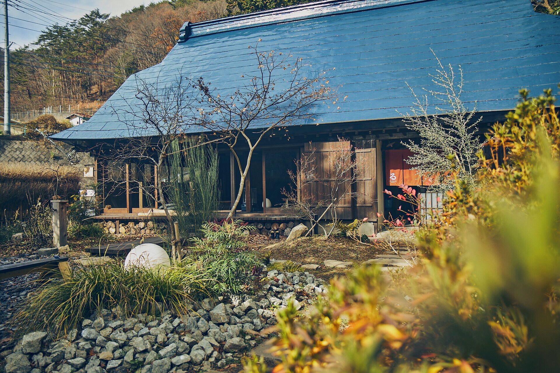 Uma casa japonesa tradicional com telhado azul, rodeada por um jardim com pedras e plantas.
